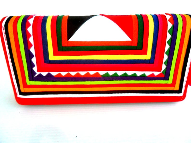 May include: A red fabric clutch purse with a colorful geometric pattern. The pattern is made up of stripes and triangles in various colors, including red, orange, yellow, green, blue, purple, and white.