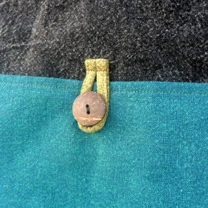 May include: A close-up of a teal blue fabric with a brown coconut button and a yellow loop. The fabric is textured and has a subtle sheen.