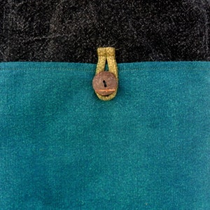 May include: A teal blue fabric bag with a brown button closure and a black fabric top.