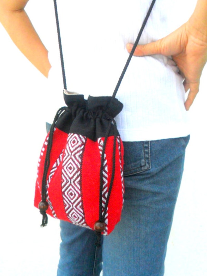 May include: A red and black woven drawstring bag with a black strap. The bag has a geometric pattern and is worn over the shoulder.