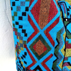 May include: A blue fabric bag with a colorful geometric pattern. The pattern features red, orange, yellow, green, and black squares and diamonds.