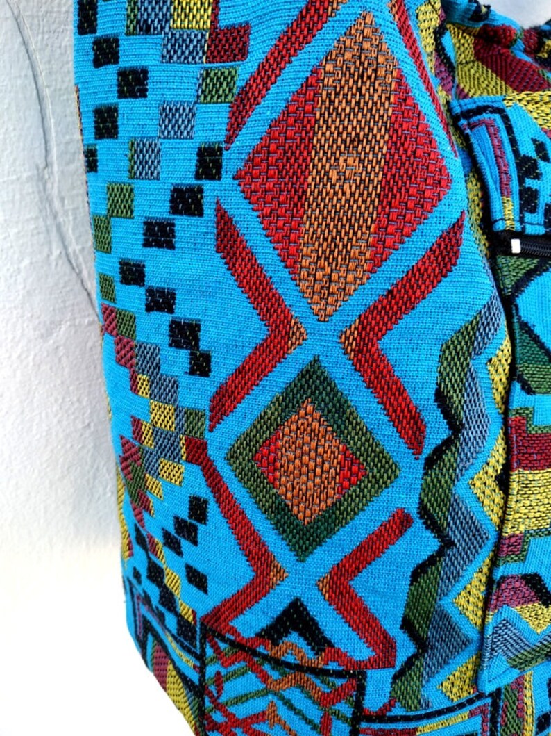 May include: A blue fabric bag with a colorful geometric pattern. The pattern features red, orange, yellow, green, and black squares and diamonds.