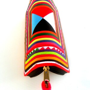 May include: A colorful zippered pouch with a geometric pattern and a pink tassel. The pouch is made of fabric and has a black zipper.