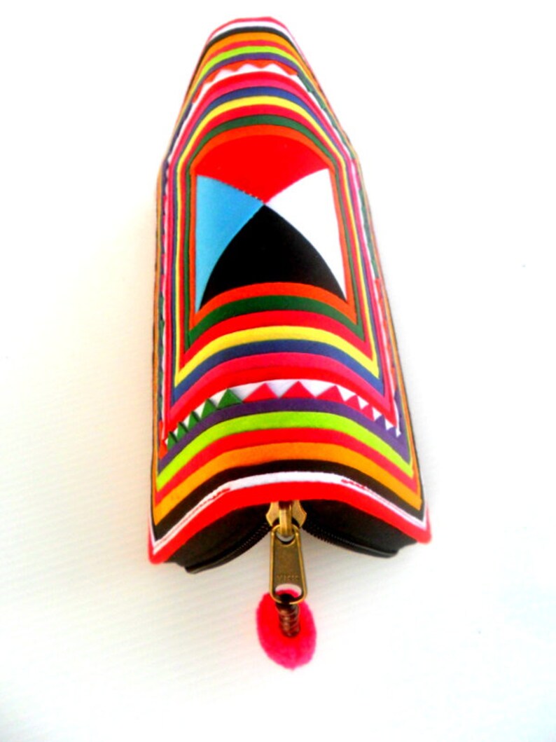 May include: A colorful zippered pouch with a geometric pattern and a pink tassel. The pouch is made of fabric and has a black zipper.