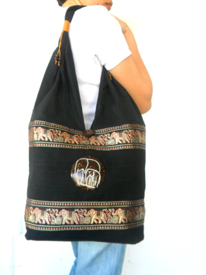 May include: A black cotton tote bag with a brown coconut shell elephant design. The bag has gold and red trim with an elephant pattern.
