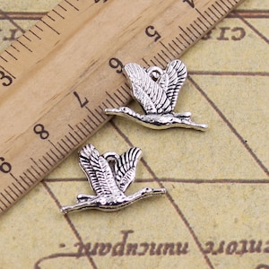 May include: Two silver-toned metal bird charms in the shape of a crane with outstretched wings. The charms are approximately 2.5 cm in length and have a loop for attaching to a necklace or bracelet.