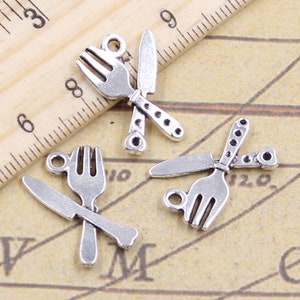 May include: Three silver-toned charms in the shape of a knife and fork, each with a loop for attaching to a necklace or bracelet.