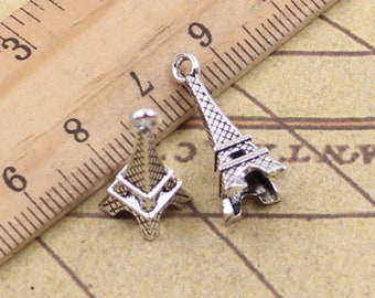 May include: Two silver Eiffel Tower charms, one with a loop for hanging, the other with a flat back. The charms are on a wooden ruler with inch markings.