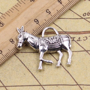 May include: Silver donkey charm with a floral design on the saddle. The charm has a loop for attaching to a necklace or bracelet.