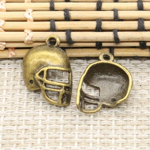 Puede incluir: Dos colgantes de casco de fútbol de color bronce. Uno es un casco completo con una máscara facial, y el otro es un contorno ahuecado. Ambos tienen un pequeño lazo en la parte superior para sujetar a joyas u otras manualidades.