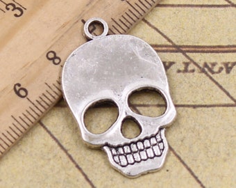 May include: Silver-toned metal skull charm pendant with a detailed design. The skull has hollow eye sockets, a nose, and a toothy grin.