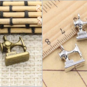 May include: Two antique gold-toned and three silver-toned miniature sewing machine charms. The charms are on a wooden surface with a ruler.