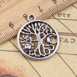 May include: Silver-toned metal charm featuring a tree of life design with a sun and moon on either side. The charm is round and has a hole at the top for hanging.