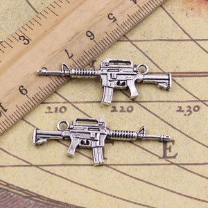 May include: Two silver-toned metal charms shaped like assault rifles. The charms are about 2 inches long and have a detailed design.
