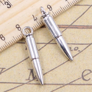 Op de afbeelding: Twee zilveren kogelcharms met een lus aan de bovenkant om aan sieraden te bevestigen. De charms zijn ongeveer 5 cm lang en hebben een realistische kogelvorm.