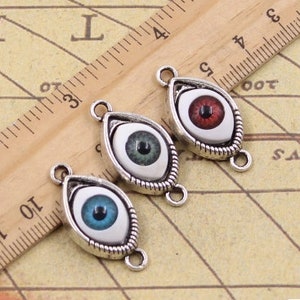 May include: Three silver eye charms with different colored eyes. The eyes are red, blue, and green. The charms are in the shape of an eye and have a silver frame.