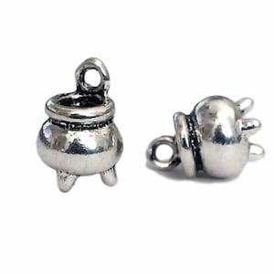 May include: Two silver charm pendants in the shape of a cauldron. The cauldron has a loop at the top for attaching to a chain or bracelet. The cauldron has three legs.