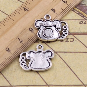 May include: Two silver-toned metal charms shaped like vintage rotary phones. Each charm has a detailed design with a dial and a curled cord.