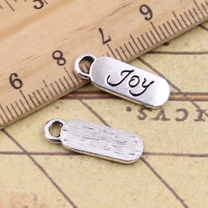 May include: Two silver charm pendants. One pendant is rectangular and has the word "Joy" engraved on it. The other pendant is plain and rectangular.