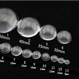 May include: A set of 13 clear glass cabochons in various sizes, ranging from 8mm to 50mm. The cabochons are arranged in order of size, with the largest cabochon at the top and the smallest cabochon at the bottom. The cabochons are all round and have a smooth, polished surface.