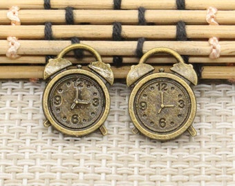 May include: Two antique gold-toned alarm clock charms with black hands and Roman numeral markings on the face.