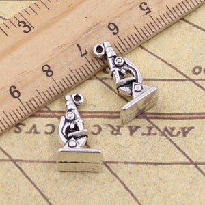 May include: Two silver microscope charms with intricate details. The charms are about 1 inch tall and have a vintage look.
