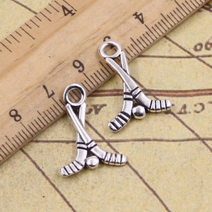 May include: Two silver-toned hockey stick charms with a small puck charm. The charms are on a ruler background.