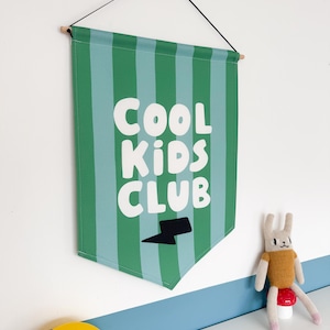 May include: Green and blue striped fabric banner with the text "COOL KIDS CLUB" in white letters and a black lightning bolt.