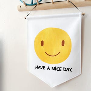 May include: White banner with a yellow smiley face and the text "HAVE A NICE DAY" in black. The banner is hanging from a wooden rod and black string.
