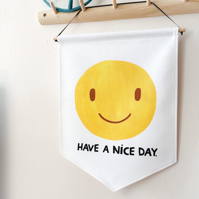May include: White banner with a yellow smiley face and the text "HAVE A NICE DAY" in black. The banner is hanging from a wooden rod and black string.