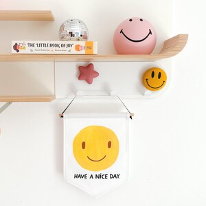 A white banner with a yellow smiley face and the text "HAVE A NICE DAY." hanging on a white wall.