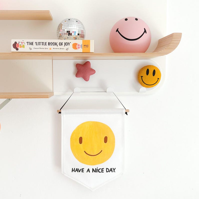 A white banner with a yellow smiley face and the text "HAVE A NICE DAY." hanging on a white wall.
