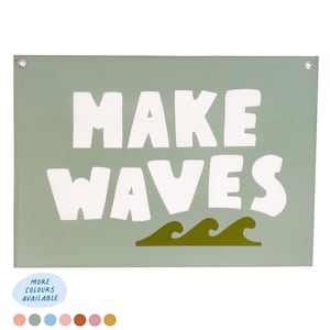 Puede incluir: Un cuadro rectangular con las palabras "MAKE WAVES" en letras blancas grandes sobre un fondo verde salvia. Debajo del texto hay tres ilustraciones de olas verdes. El arte tiene ojales metálicos en cada esquina.