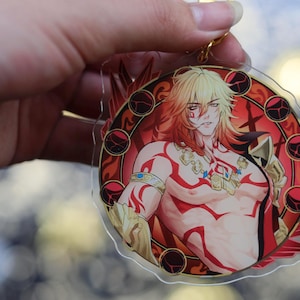 May include: A clear acrylic keychain featuring a muscular anime-style character with blonde hair and red markings. The character is set against a red and gold circular design. A gold-colored keyring is attached.