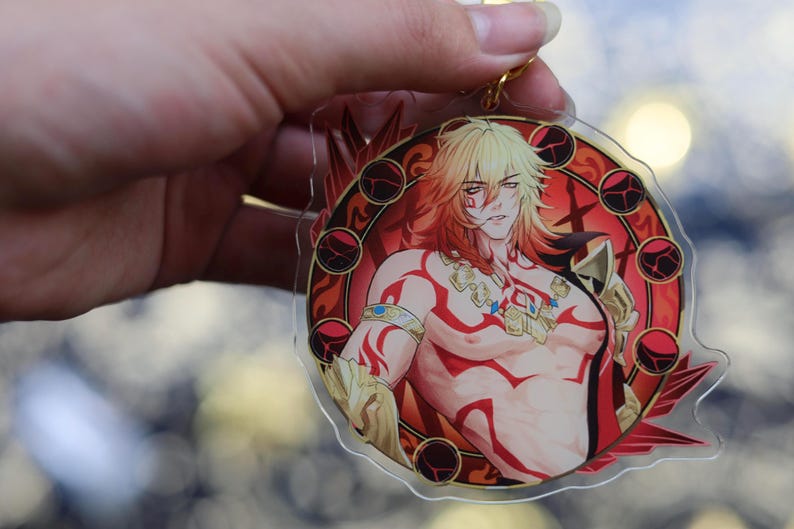 May include: A clear acrylic keychain featuring a muscular anime-style character with blonde hair and red markings. The character is set against a red and gold circular design. A gold-colored keyring is attached.