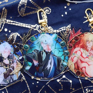 May include: Three anime-style acrylic keychains with gold-colored clasps. Each keychain features a different character illustration with vibrant colors and intricate details. The background is a dark blue fabric with gold celestial patterns.