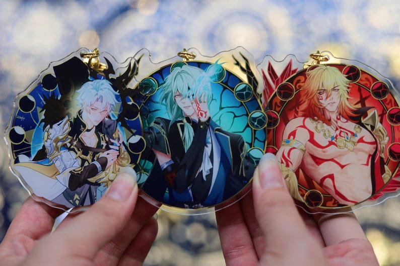 May include: Three anime-style acrylic charms featuring male characters. Each charm has a circular design with a gold-colored top loop. The characters have different hair colors and outfits, set against colorful backgrounds with decorative borders.