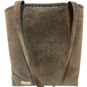 K&ouml;nnte beinhalten: Eine braune Ledertasche mit zwei Henkeln. Die Tasche hat eine strukturierte Oberfl&auml;che und ein kleines Etikett mit der Aufschrift "Handmade".