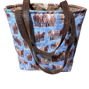 K&ouml;nnte beinhalten: Eine blaue Tragetasche mit braunen Lederriemen und einem Pferde-Druckmuster. Die Tasche ist aus Stoff und hat einen Rei&szlig;verschluss.