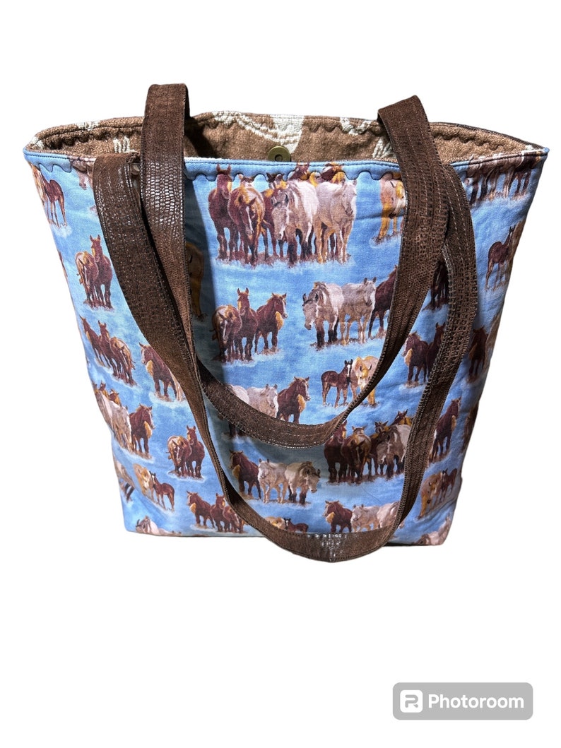 K&ouml;nnte beinhalten: Eine blaue Tragetasche mit braunen Lederriemen und einem Pferde-Druckmuster. Die Tasche ist aus Stoff und hat einen Rei&szlig;verschluss.