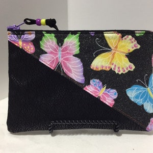 May include: A black zippered pouch with a black leather-like bottom and a top section with a black background and a colorful butterfly print. The zipper pull has purple and yellow beads.
