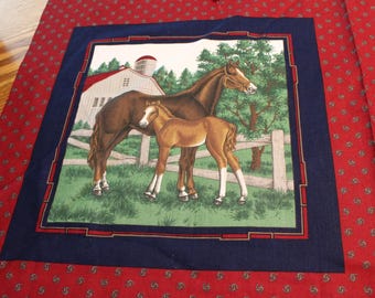 May include: A fabric panel featuring a detailed illustration of a brown horse and a foal standing in a grassy field near a white barn and fence. The illustration is framed by a navy blue border and a red paisley pattern.
