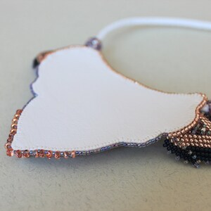 May include: A white beaded necklace with a copper and black beaded design. The necklace is in the shape of a crescent moon.