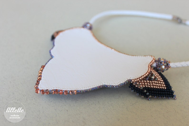May include: A white beaded necklace with a copper and black beaded design. The necklace is in the shape of a crescent moon.