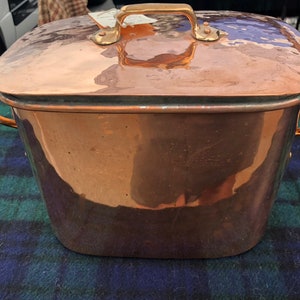 May include: A large copper pot with a lid and two brass handles. The pot is oval shaped and has a hammered finish.