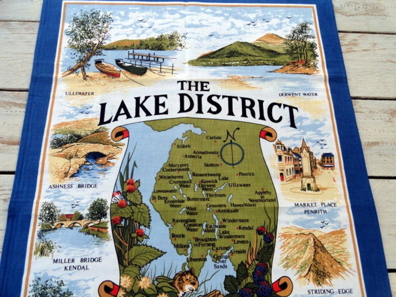 May include: A colorful tea towel with a map of the Lake District in England. The map shows the location of various towns and lakes, including Ullswater, Derwent Water, and Keswick Lake. The tea towel also features illustrations of bridges, mountains, and other landmarks.
