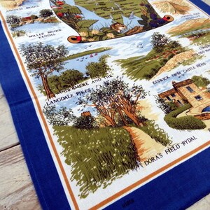 May include: A blue and white tea towel with a map of the Lake District in England. The map features various landmarks and locations, including Windermere and the Langdale Pikes, Keswick from Castle Head, and Dora's Field Rydal. The tea towel has a blue border and a brown and white pattern.