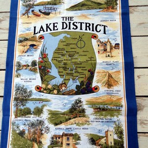 May include: A blue tea towel with a map of the Lake District in England. The map shows the locations of various towns, lakes, and mountains. The text "The Lake District" is printed in large letters at the top of the towel.