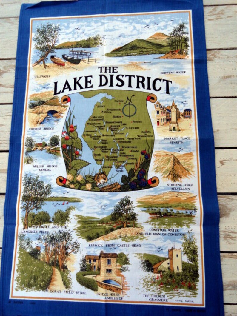 May include: A blue tea towel with a map of the Lake District in England. The map shows the locations of various towns, lakes, and mountains. The text "The Lake District" is printed in large letters at the top of the towel.