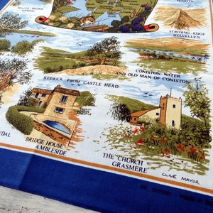May include: A white tea towel with a blue border features a colorful illustration of the Lake District in England. The illustration includes landmarks like Helvellyn, Coniston Water, and Grasmere. The text "all cotton made in Britain" is printed in the bottom right corner.